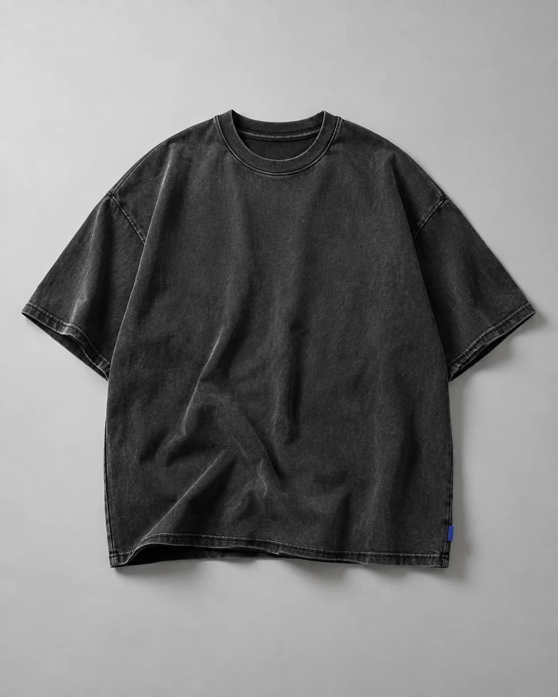 Washed-black oversized heavyweight T-shirt on a cool grey studio backdrop